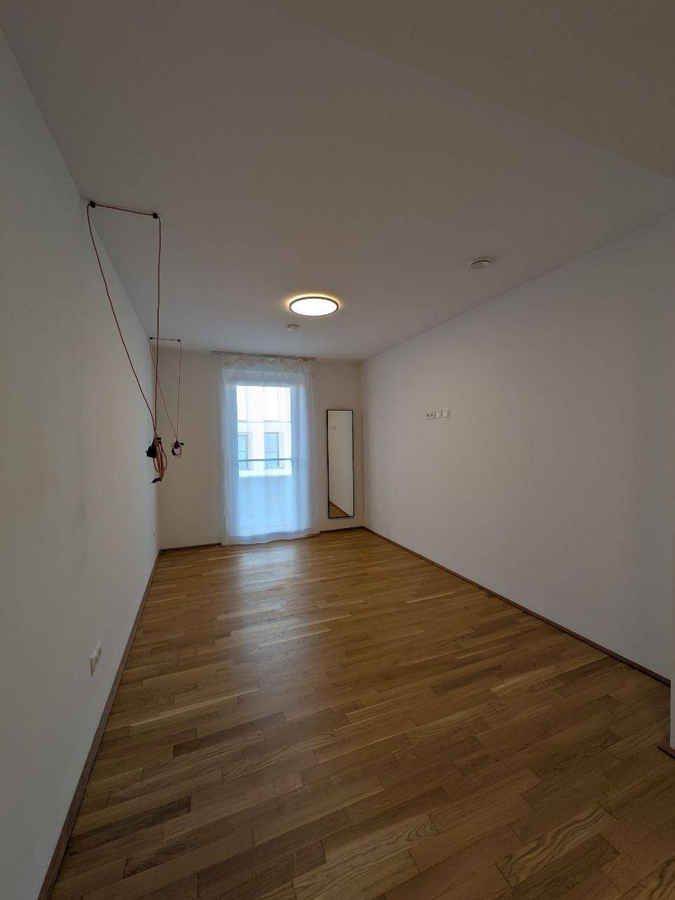 Heller, leerer Raum mit Fenster, Holzfußboden und weiß gestrichenen Wänden.