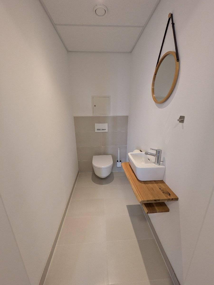 Modernes Gäste-WC mit Wand-WC, kleinem Waschbecken und Holzablage.