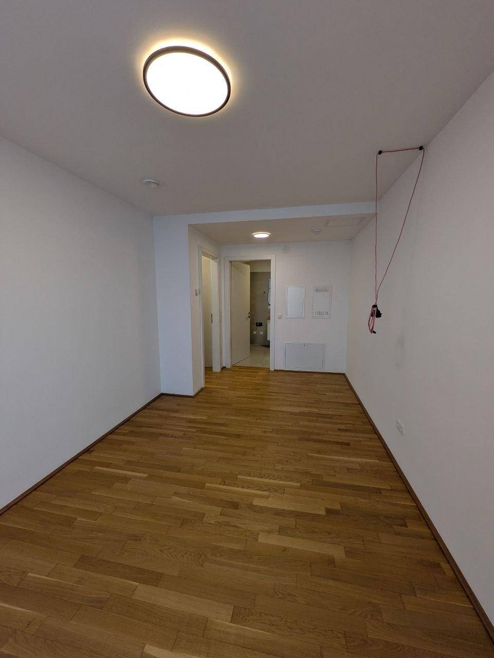Leerer Raum mit hellem Holzfußboden und weiß gestrichenen Wänden.