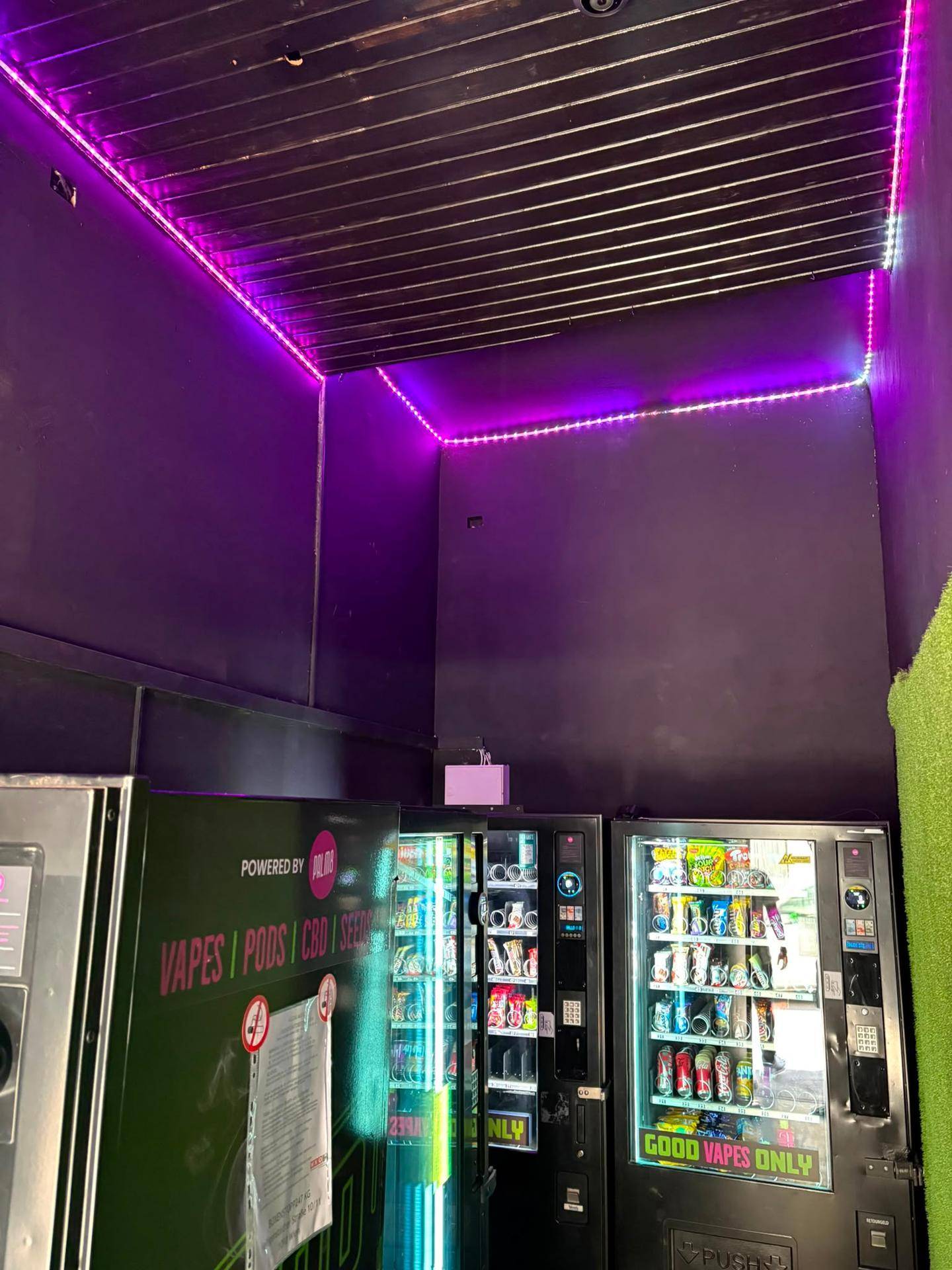 Innenraum eines Snack-Shops mit Verkaufsautomaten und lila LED-Beleuchtung an der Decke.