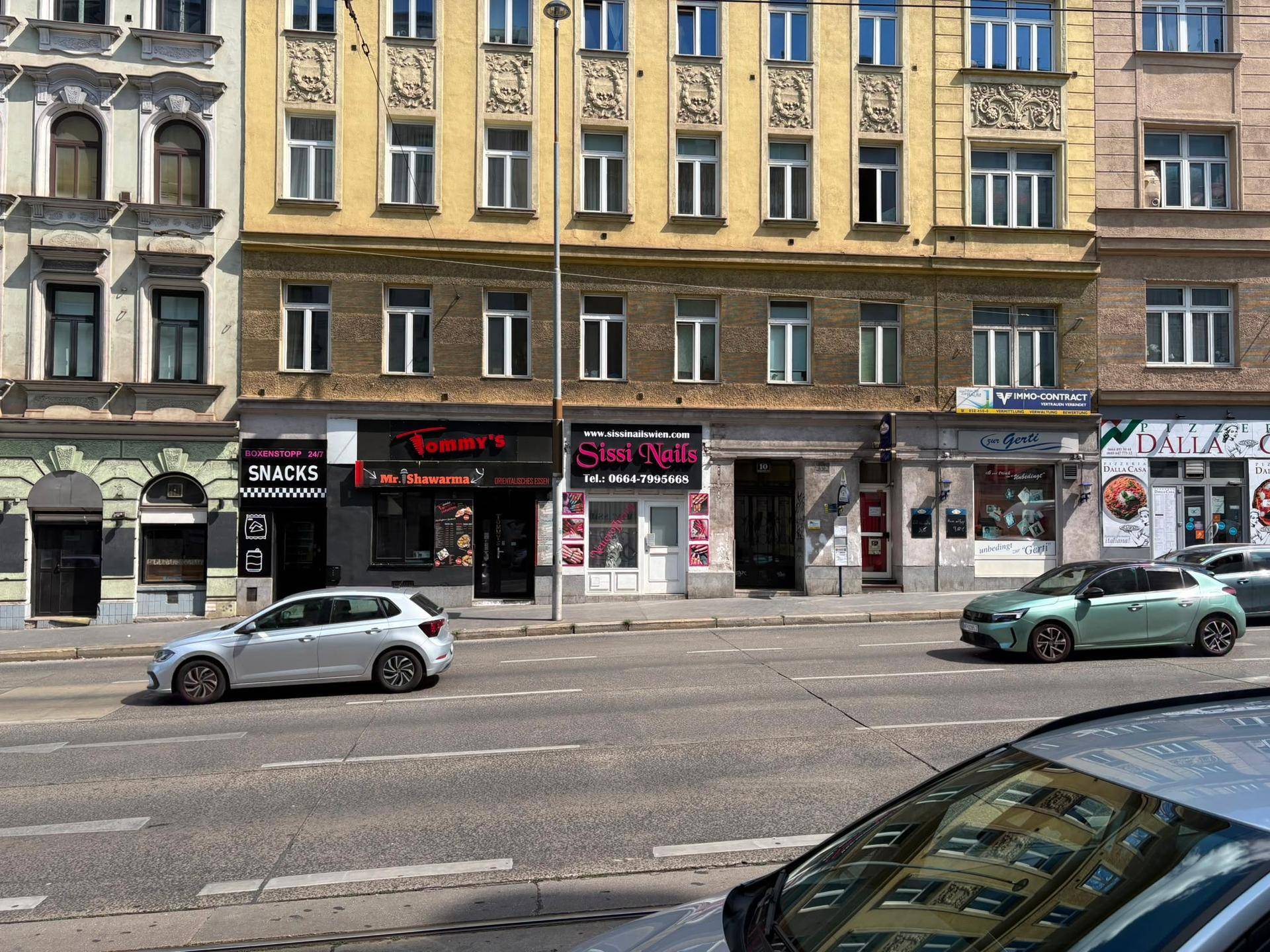 Blick auf eine belebte Straße mit verschiedenen Geschäften und geparkten Autos.