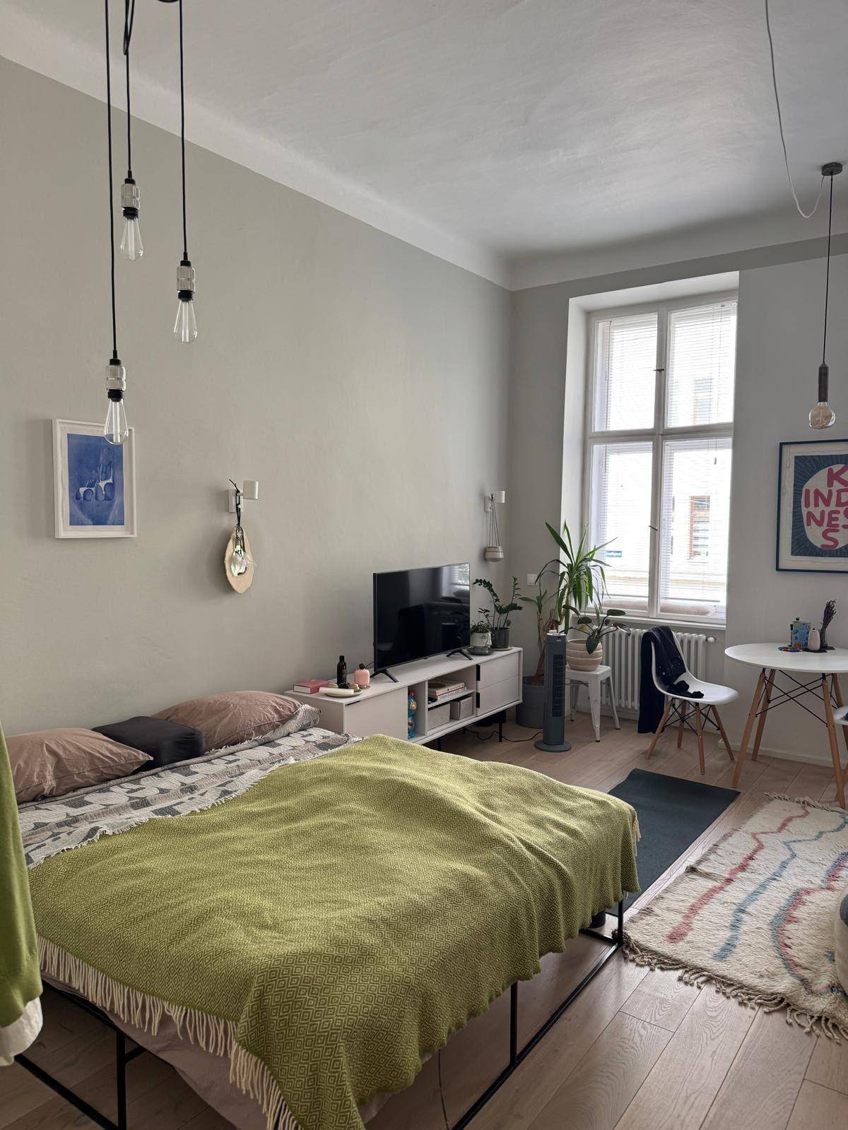 Gemütlicher Wohnbereich mit Bett, Fernseher und einem Fenster, das viel Licht hereinlässt.