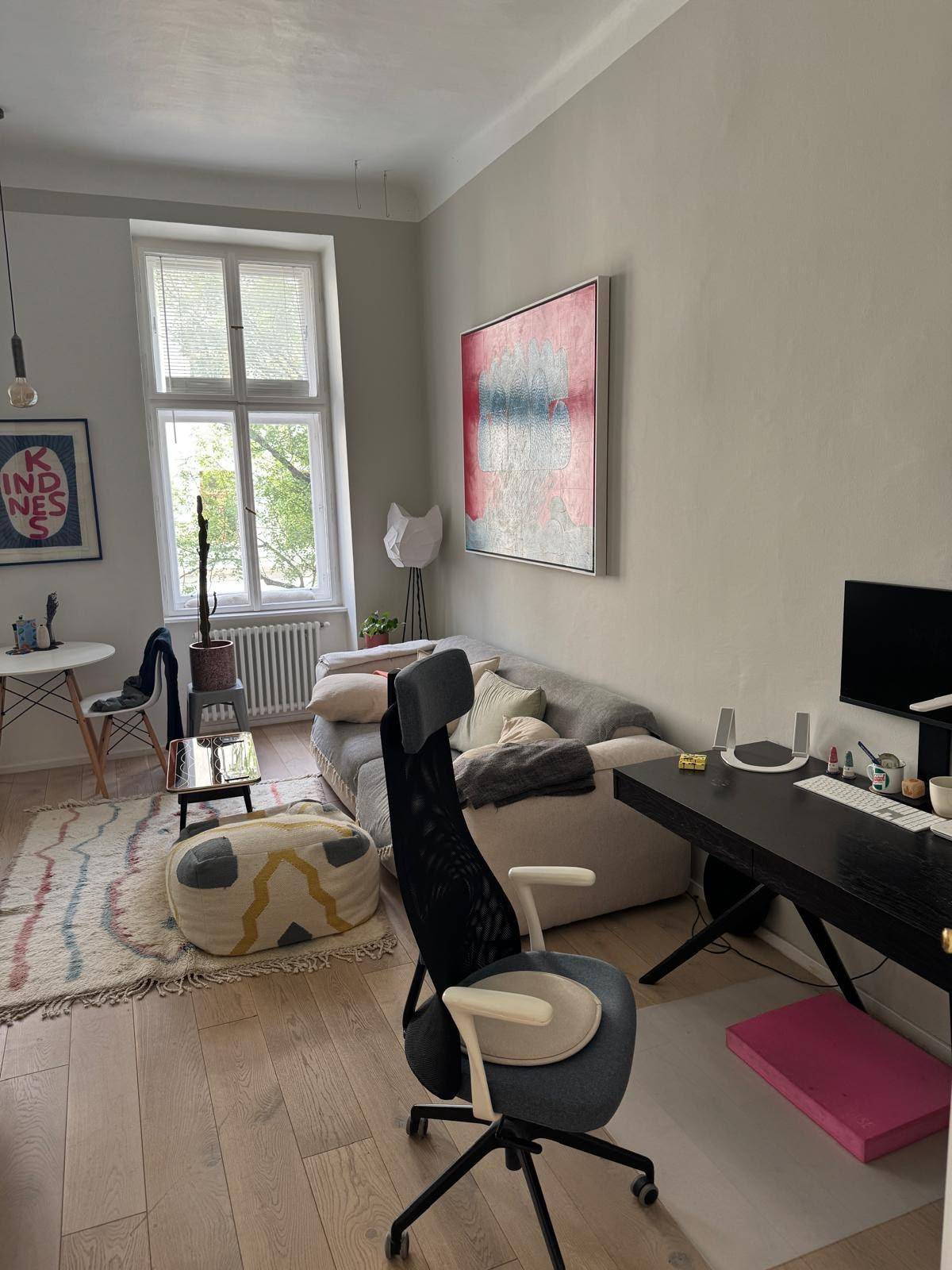 Heller Wohnbereich mit Sofa, Schreibtisch und einem großen Fenster mit Blick ins Grüne.