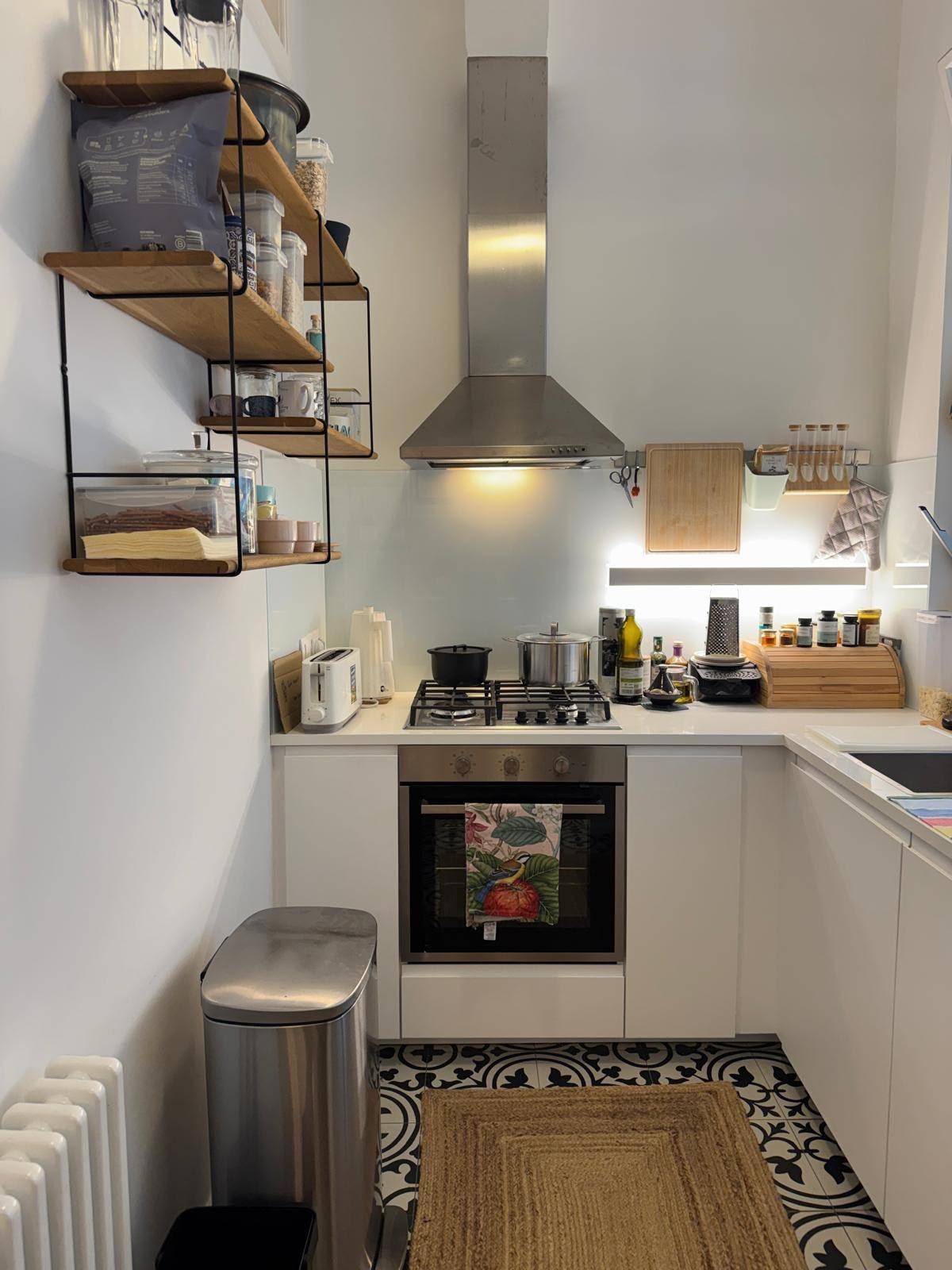 Kleine, funktionale Küche mit weißen Schränken, Herd und dekorativen Bodenfliesen.