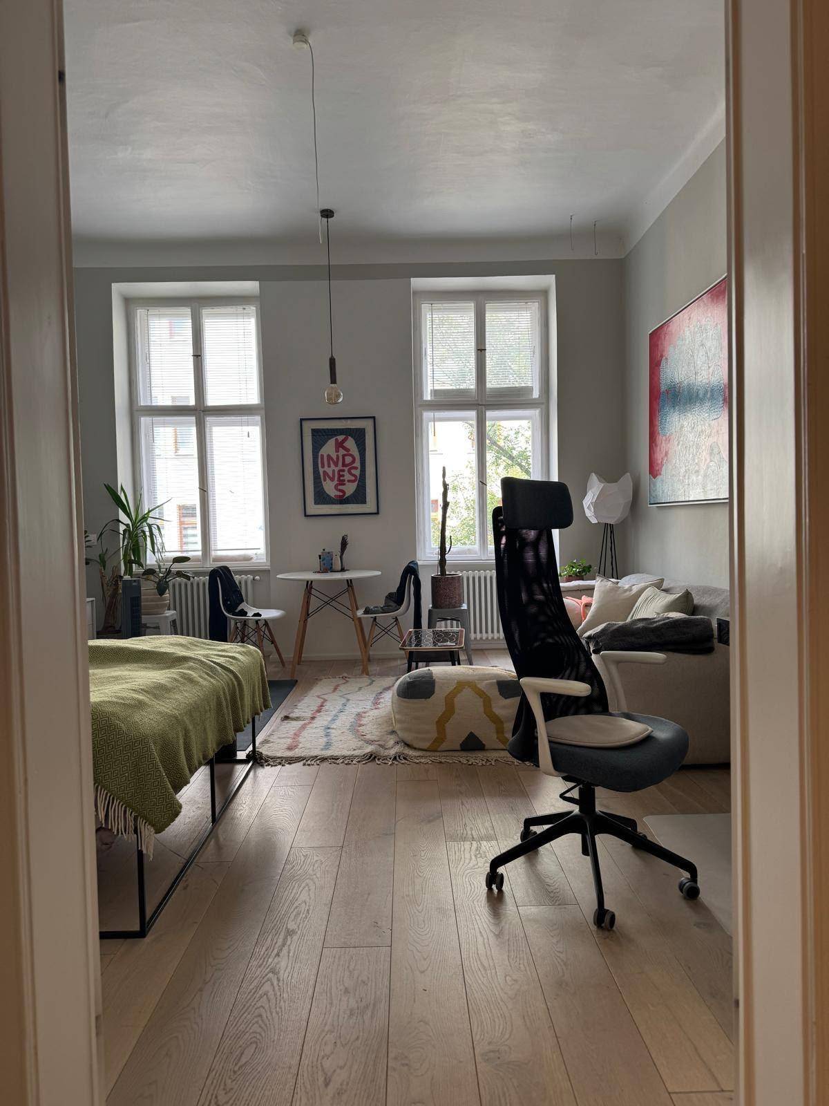 Geräumiger Wohnbereich mit Holzboden, zwei großen Fenstern und moderner Einrichtung.