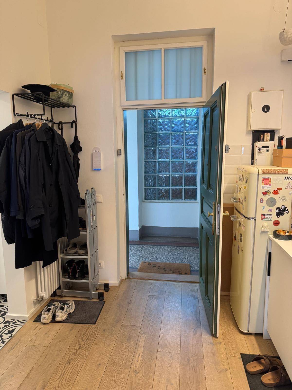 Eingangsbereich mit Garderobe, Kühlschrank und einer Tür mit Glasbausteinen.