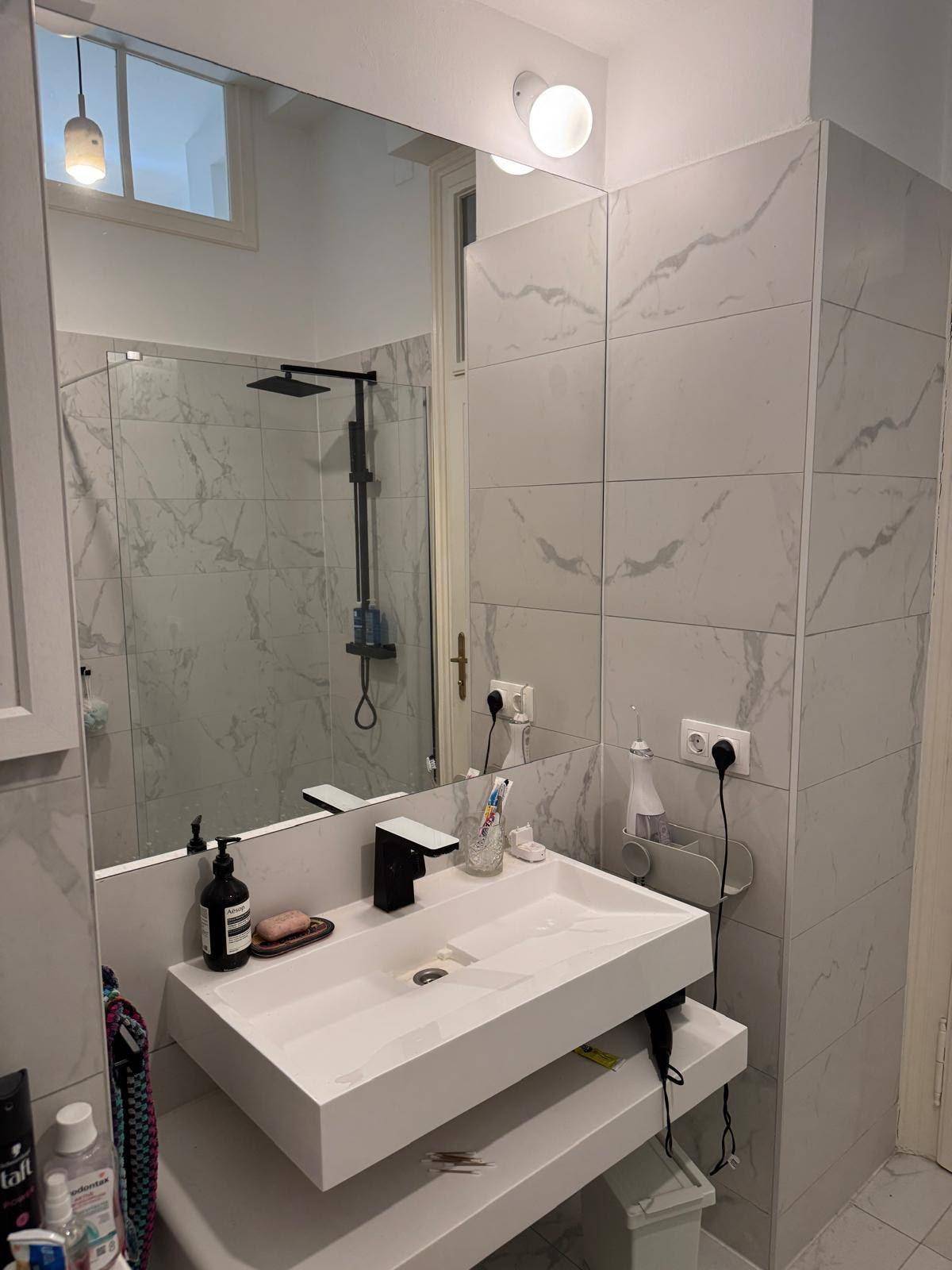 Helles Badezimmer mit modernem Waschbecken, großem Spiegel und Duschbereich.