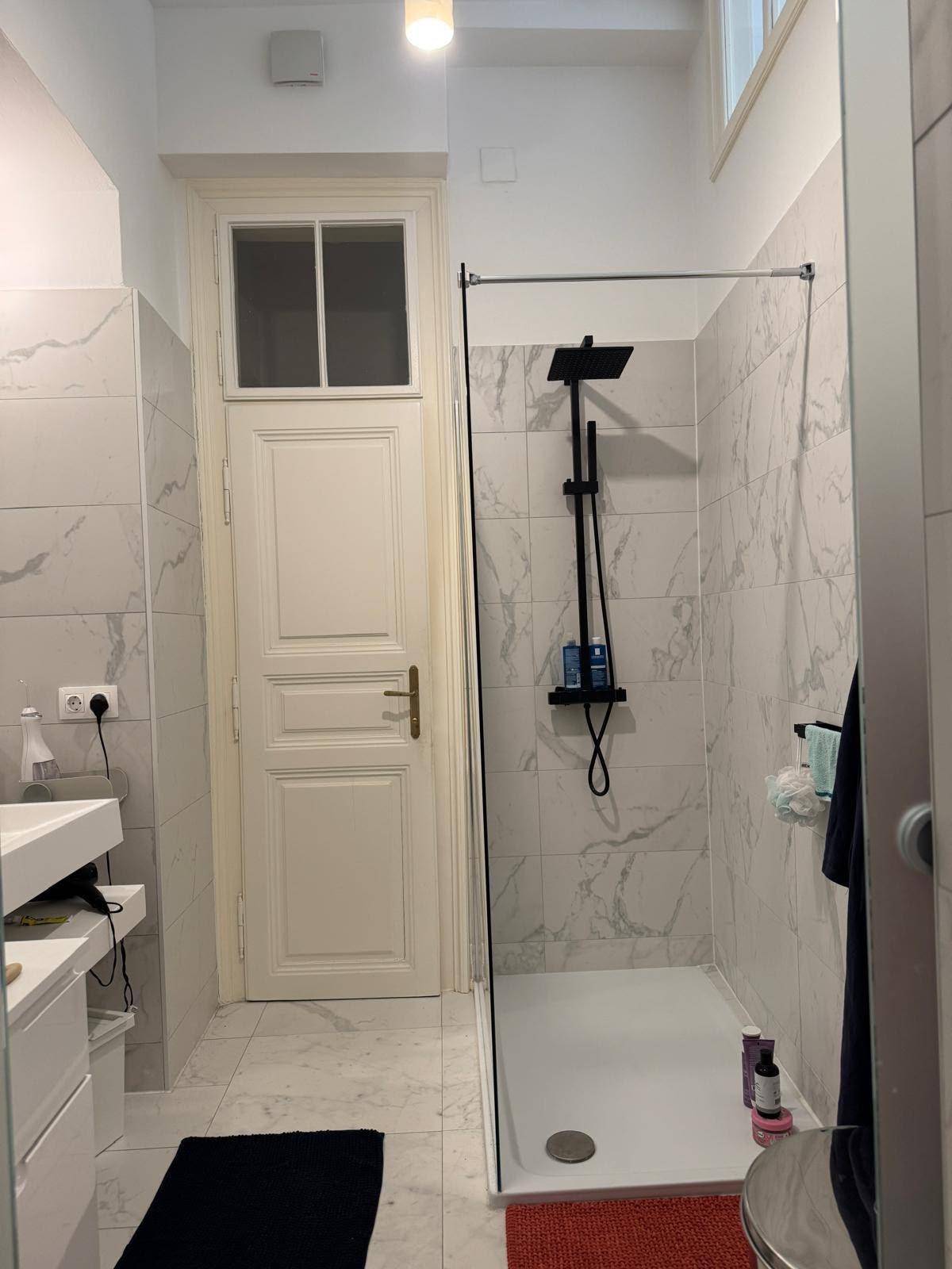 Modernes Badezimmer mit begehbarer Dusche, weißen Fliesen und einer hohen Tür.