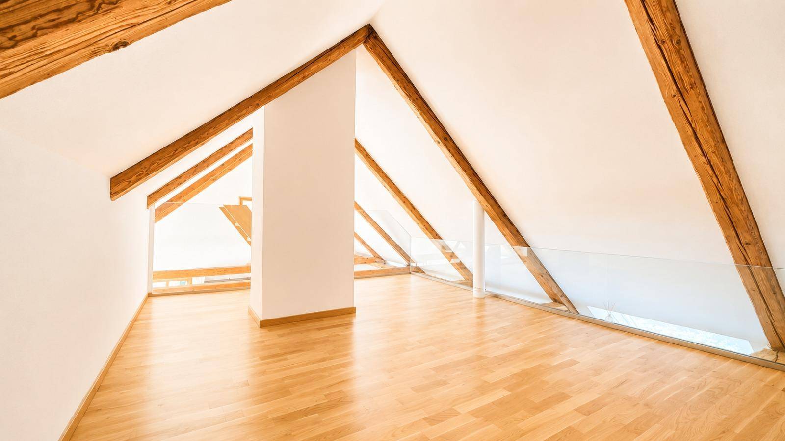 Heller Dachbodenraum mit schrägen Decken, Holzbalken und Glasgeländer, das Offenheit schafft.