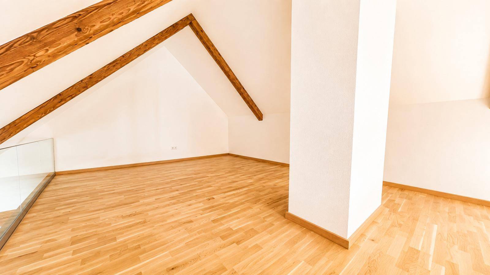 Leerer Dachbodenraum mit schrägen Decken, sichtbaren Holzbalken und hellem Holzfußboden, vielseitig nutzbar.