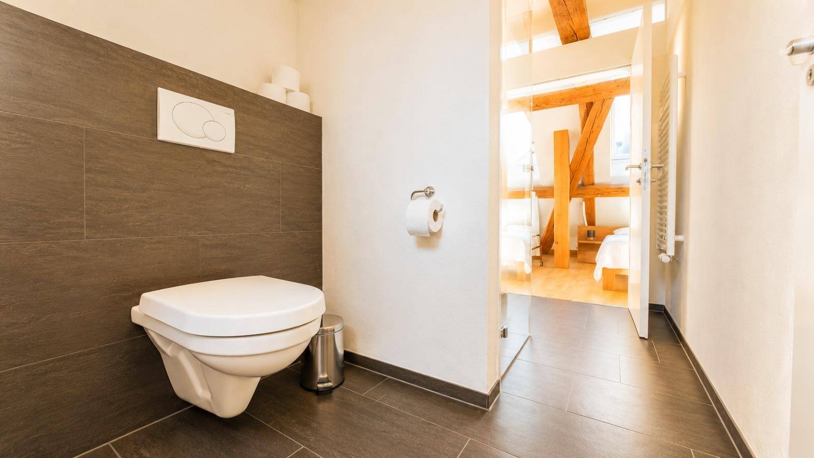 Separates WC mit wandhängender Toilette und dunklen Fliesen, praktisch und modern gestaltet.