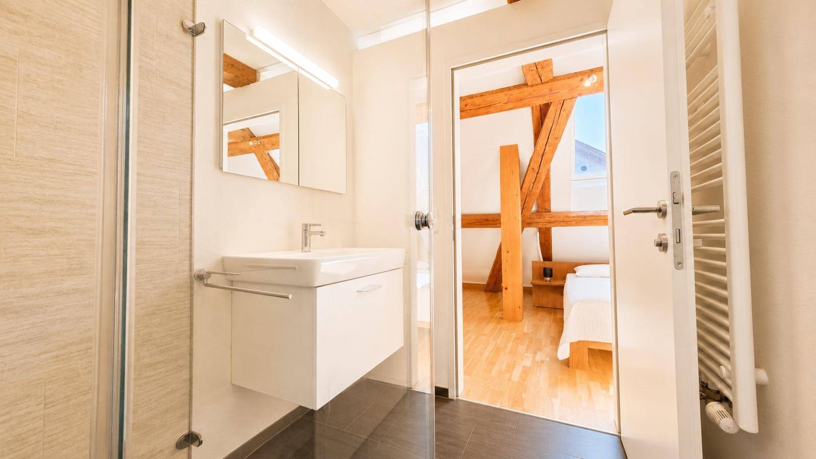 Helles Badezimmer mit Einzelwaschbecken, Spiegelschrank und beheiztem Handtuchhalter, direkt vom Schlafzimmer zugänglich.