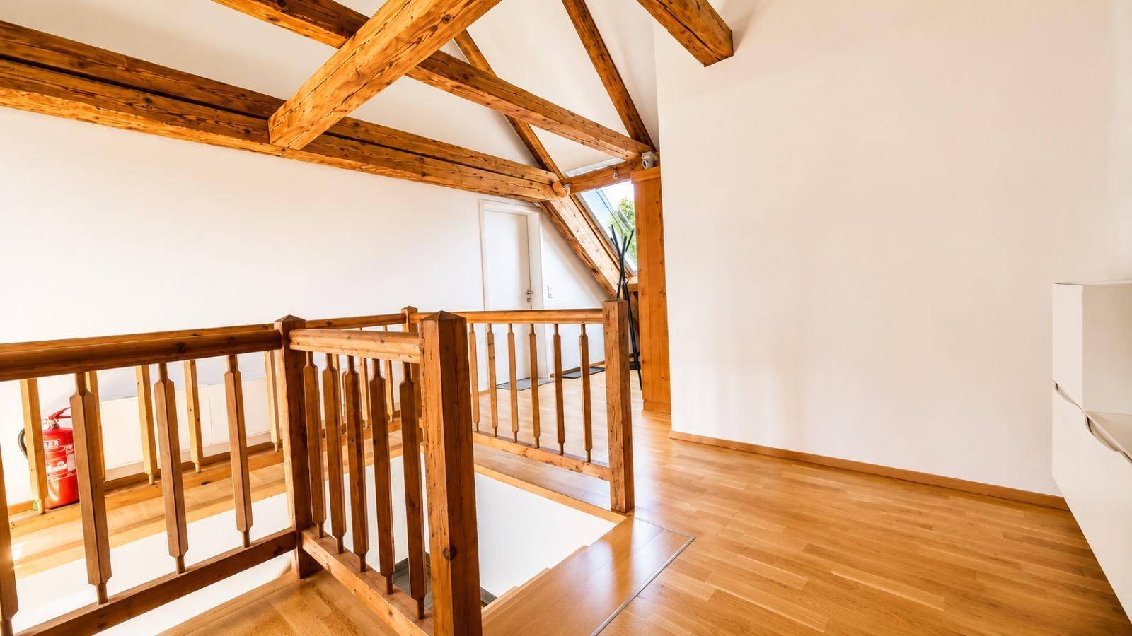 Holztreppengeländer führt in die untere Etage, mit hellem Holzfußboden und weiß gestrichenen Wänden.