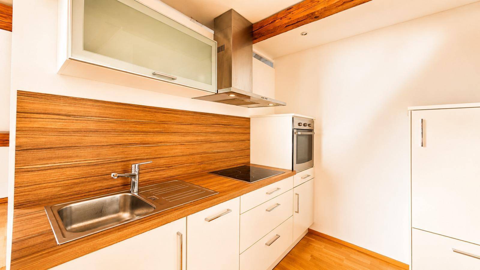 Moderne, kompakte Küche mit weißen Schränken, Holzdetails, Induktionskochfeld und integriertem Backofen.
