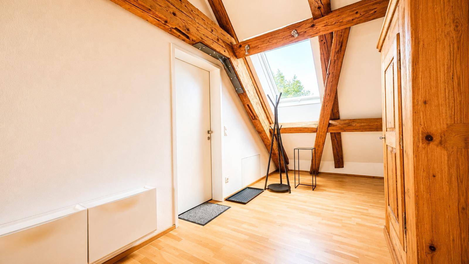 Heller Flurbereich im Dachgeschoss mit Garderobe, Schrank und Dachfenster, das Tageslicht hereinlässt.