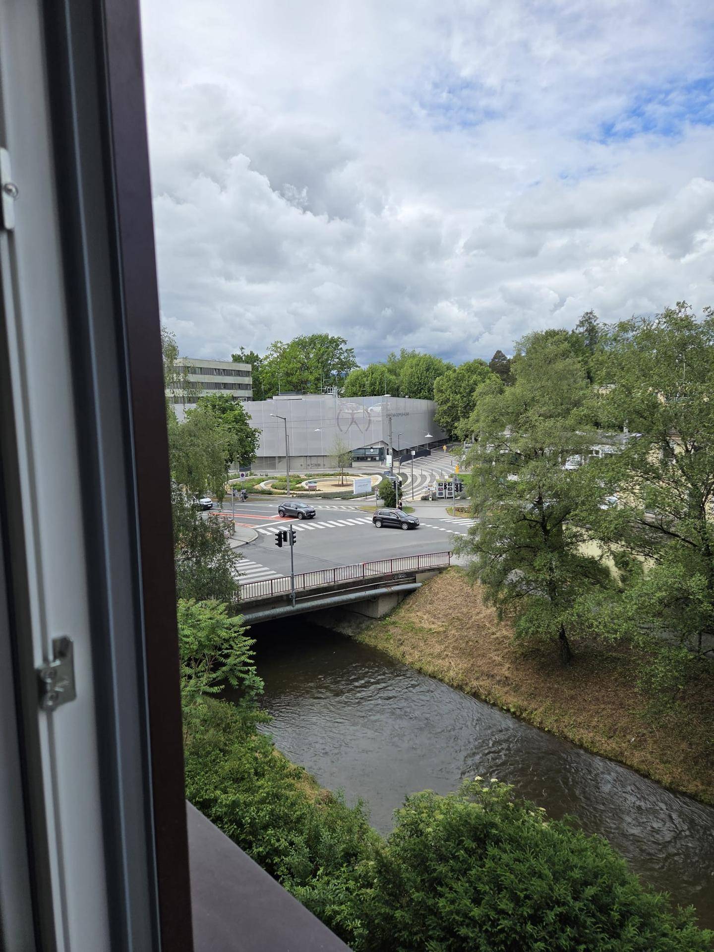 Ausblick aus dem Fenster auf eine belebte Straße, eine Brücke und einen Fluss mit viel Grün.