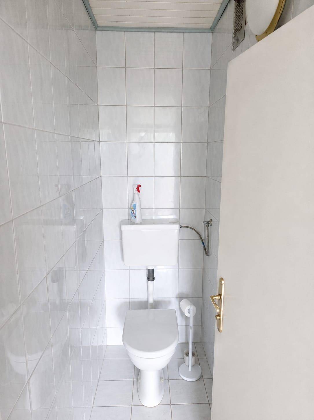 Separates WC mit weißer Toilette und hellen Fliesen an Wänden und Boden, sauber und funktional.