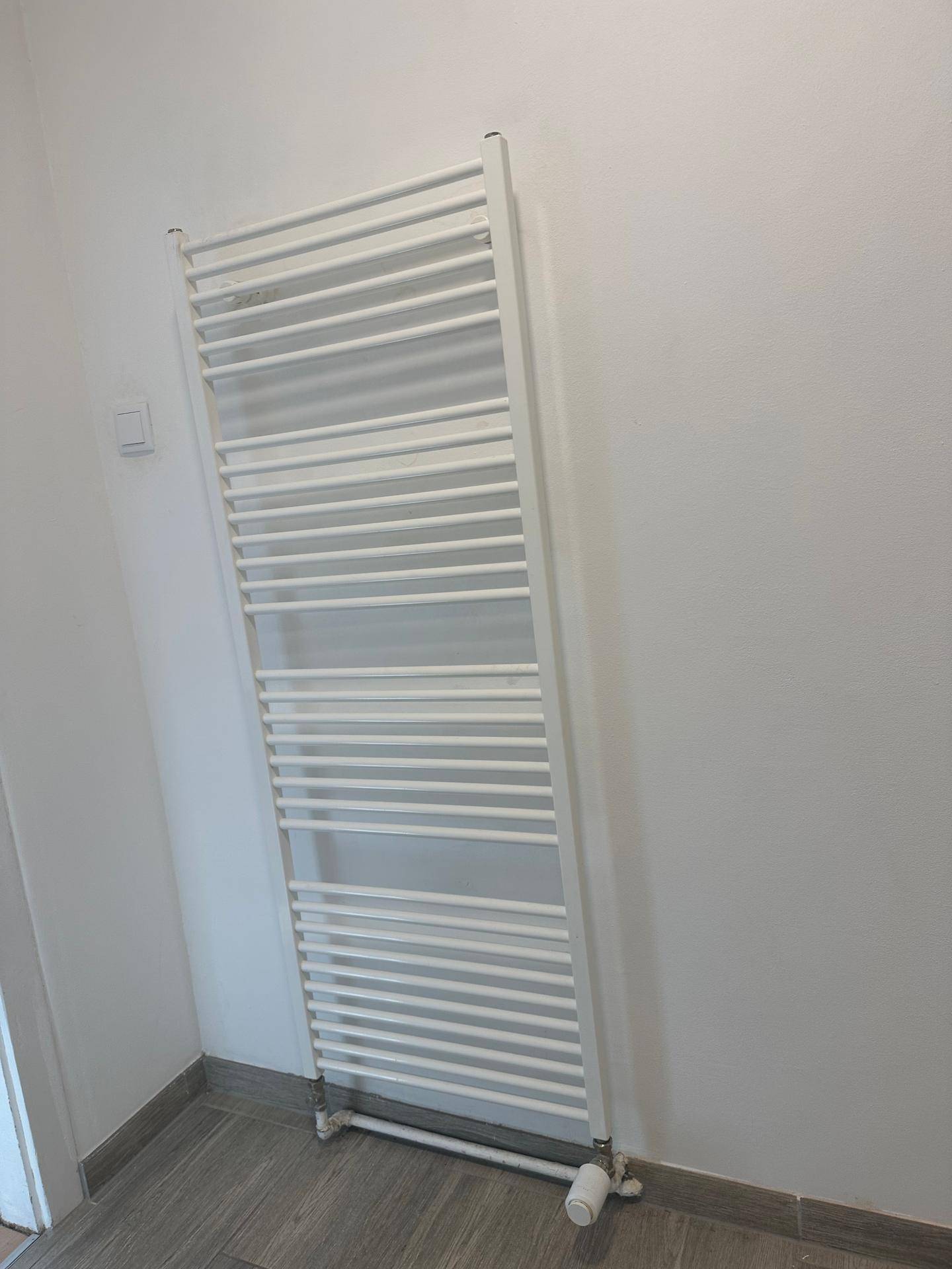 Weißer Handtuchheizkörper an einer hellen Wand in einem Badezimmer.