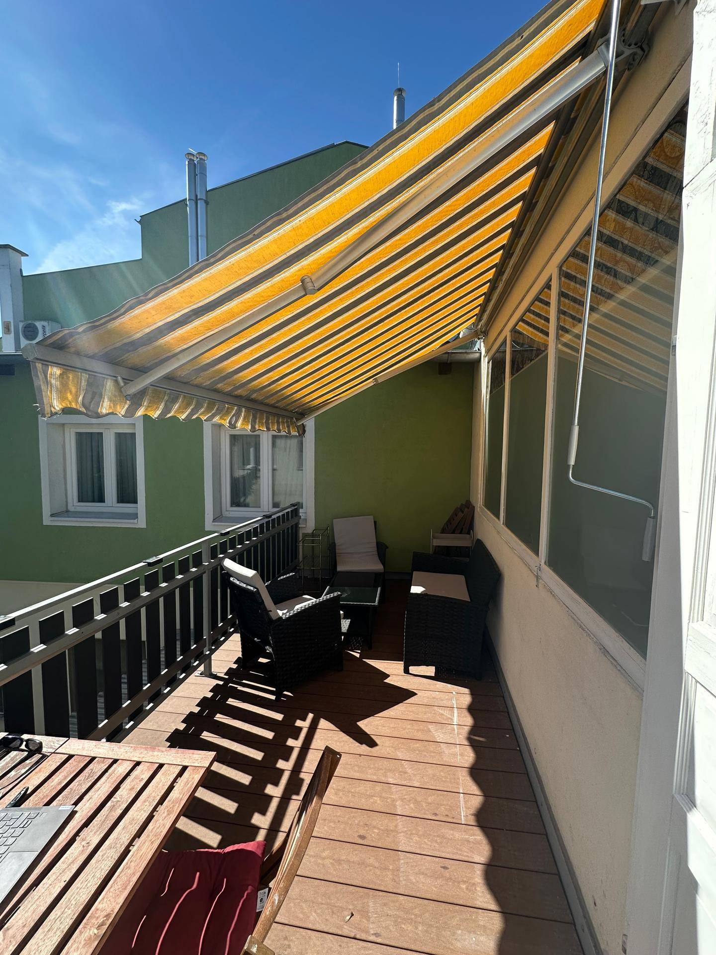 Sonniger Balkon mit Holzboden, Markise und bequemen Sitzmöbeln, ideal zum Entspannen im Freien.