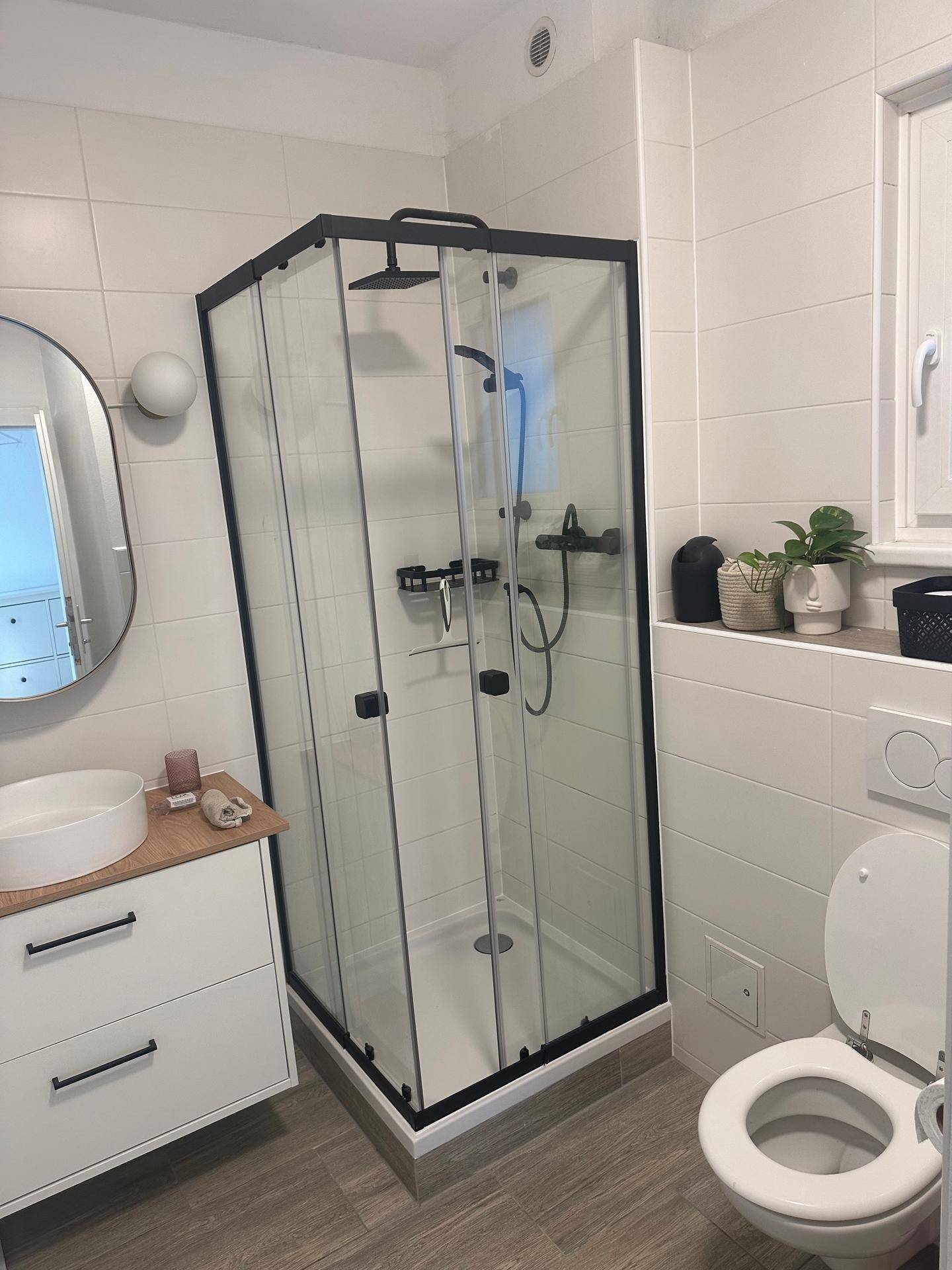Helles Badezimmer mit moderner Duschkabine, WC und Fenster für natürliche Belüftung.