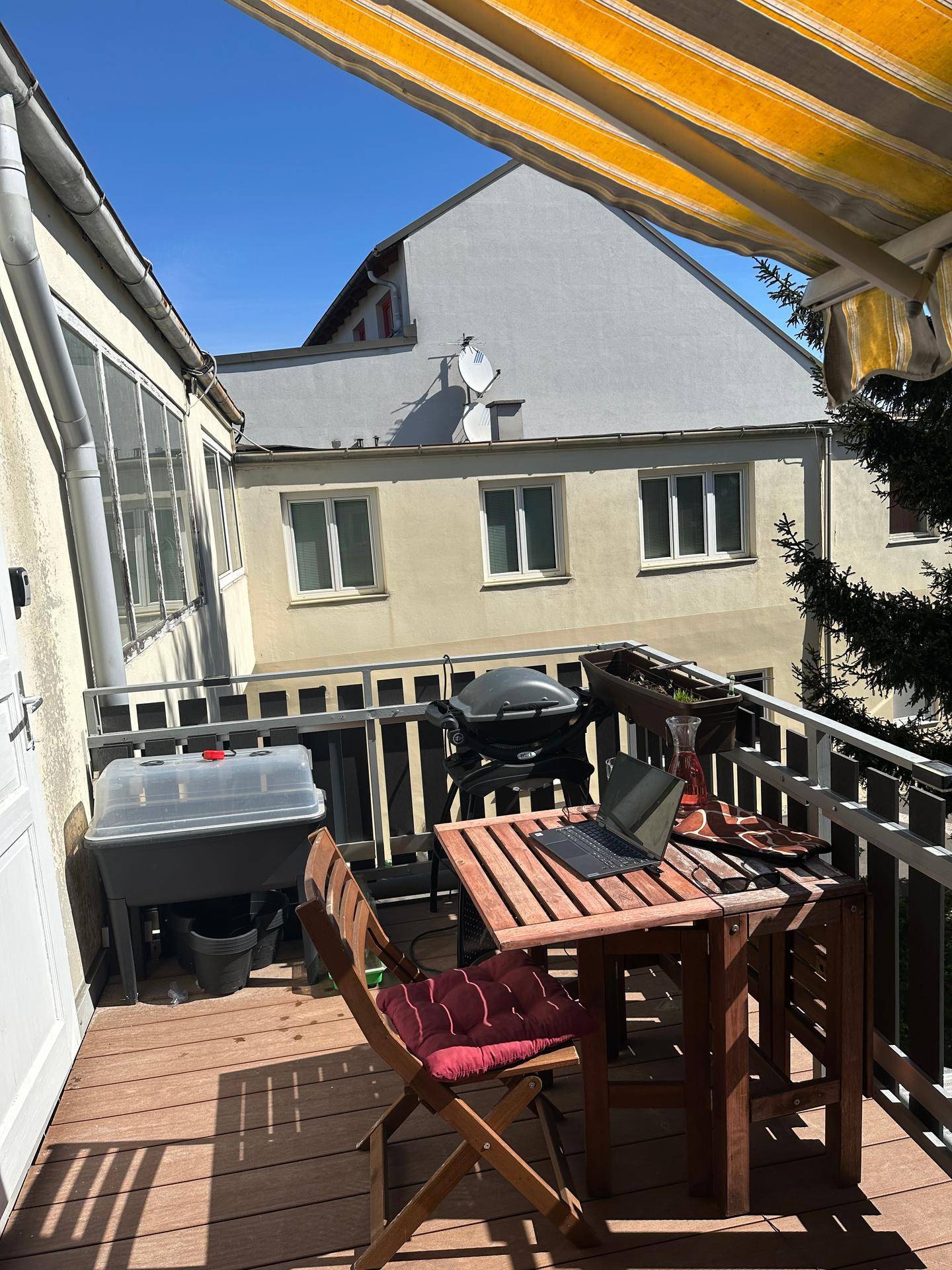 Gemütlicher Balkon mit Holztisch, Grill und Markise, perfekt für Mahlzeiten im Freien.