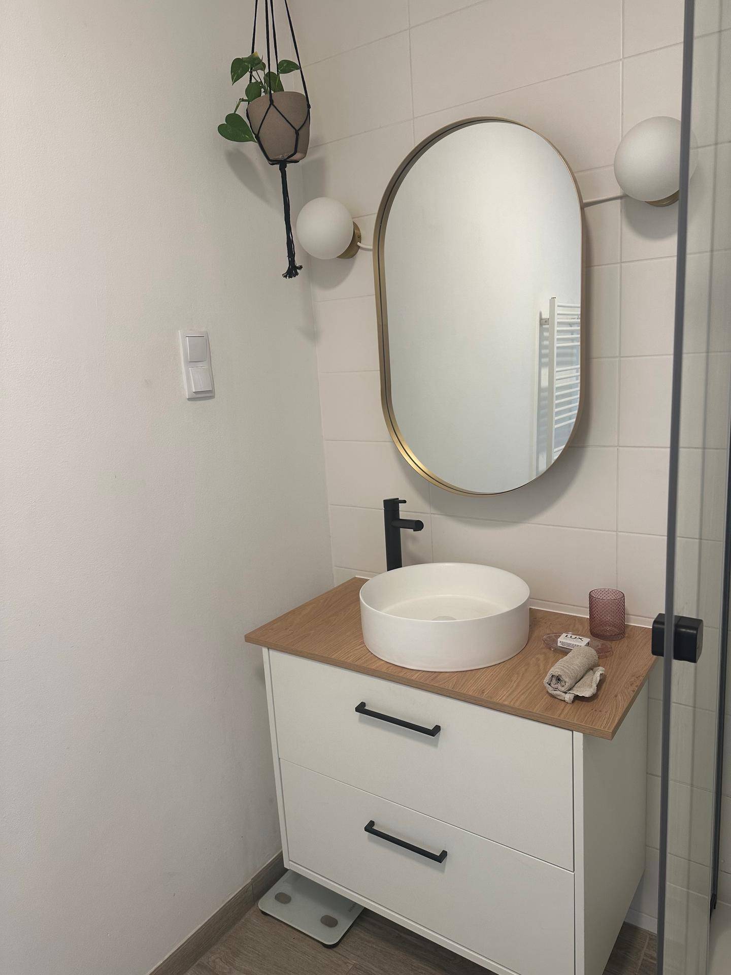 Modernes Badezimmer mit ovalem Spiegel, Aufsatzwaschbecken und Holzwaschtisch.
