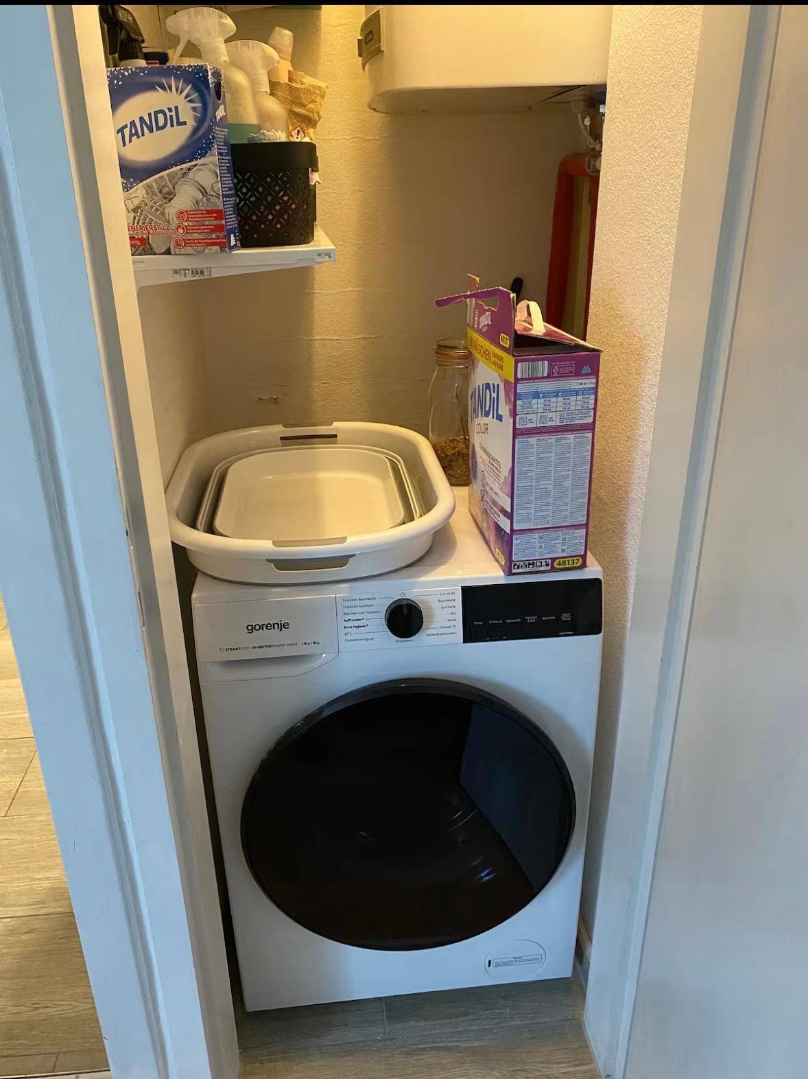 Kleiner Hauswirtschaftsraum mit Waschmaschine und Regalen für Reinigungsutensilien.
