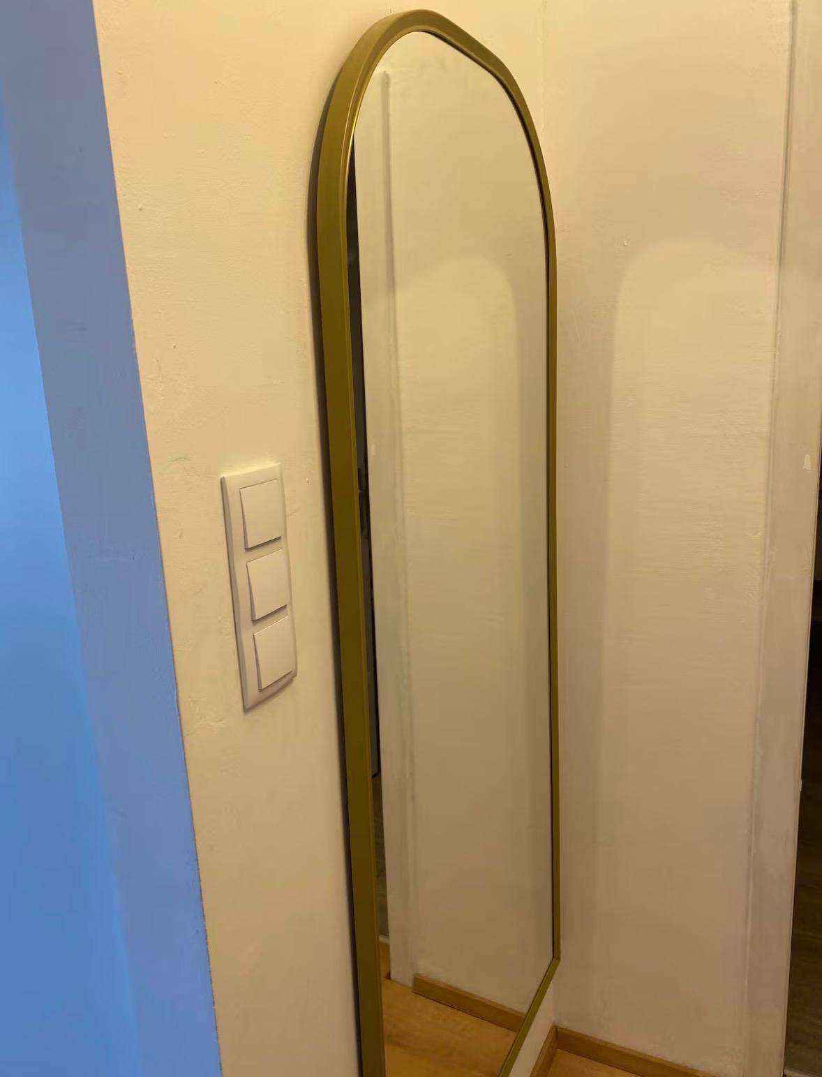 Langer, schmaler Spiegel mit goldenem Rahmen an einer weißen Wand im Flur.