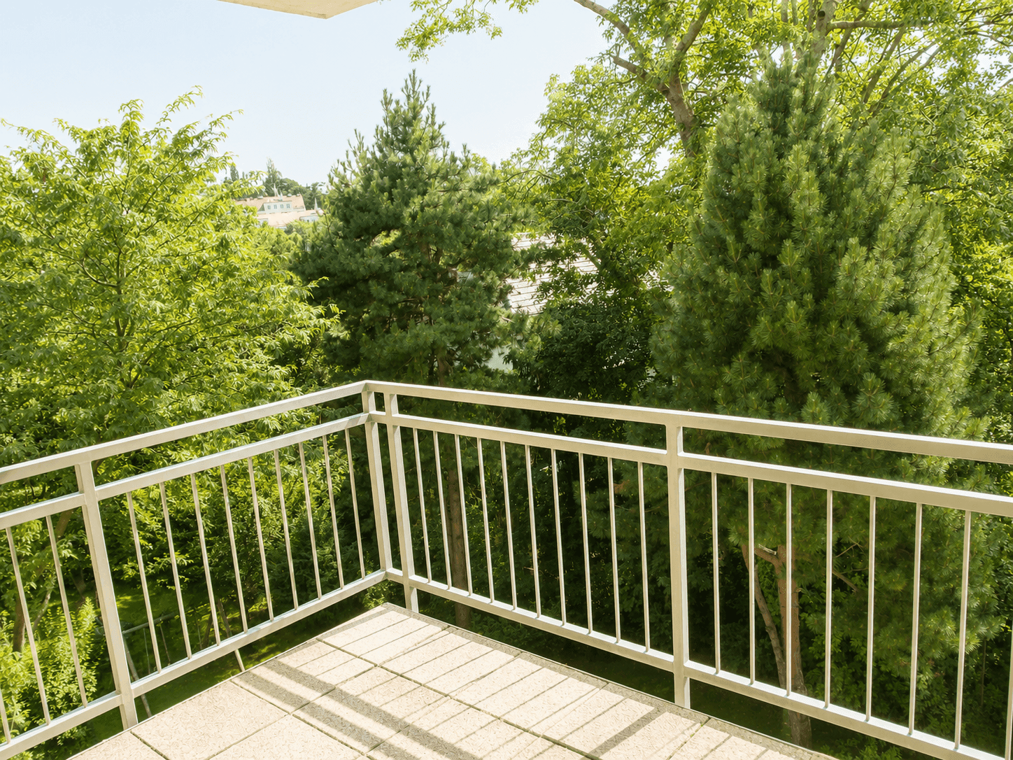 Balkon mit weißem Geländer und weitem Blick ins Grüne, umgeben von Bäumen.