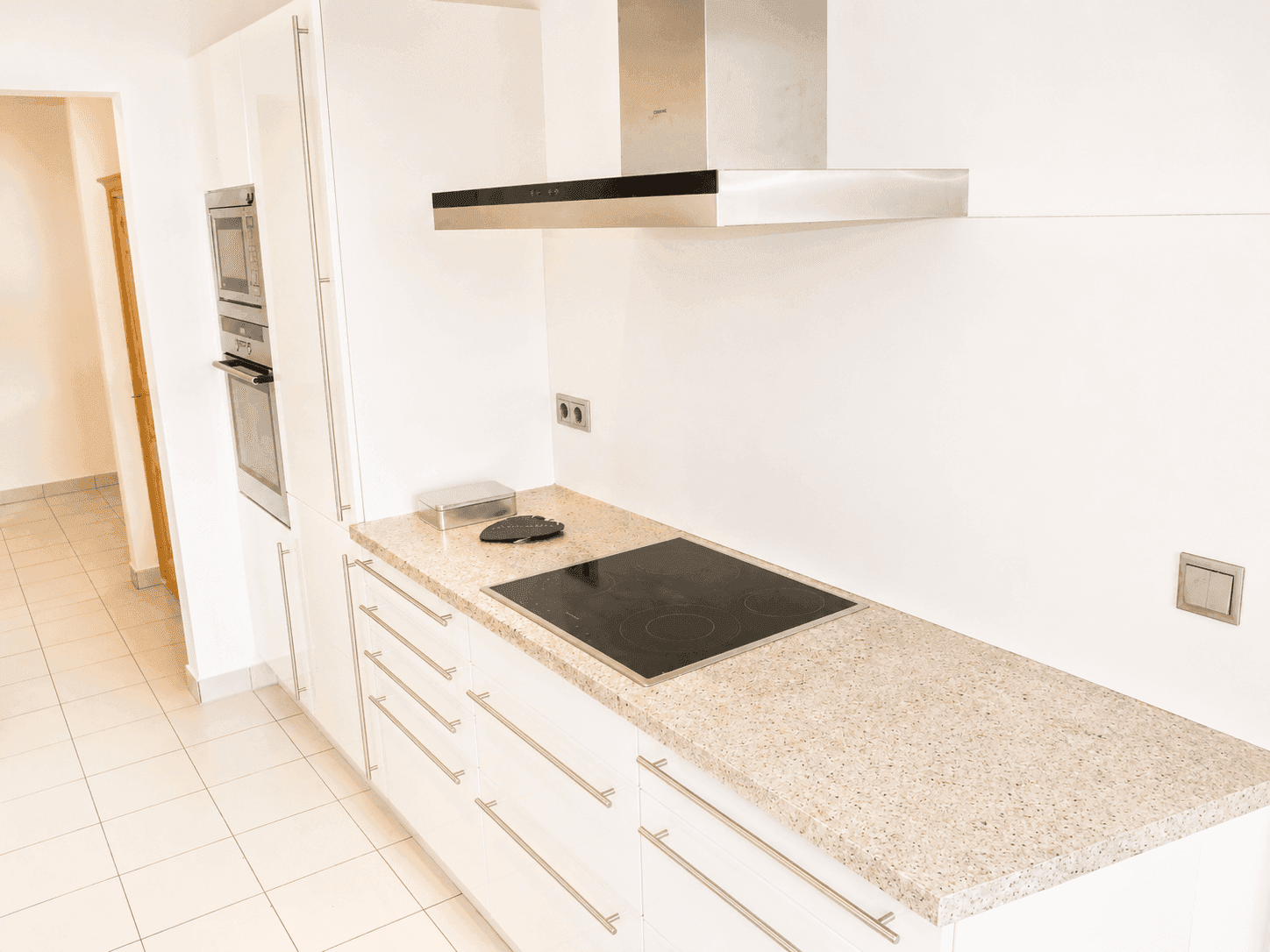 Helle Küche mit Induktionskochfeld, Dunstabzugshaube und Backofen in Hochschrank.