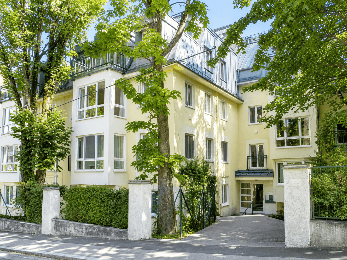 Attraktives Mehrfamilienhaus mit heller Fassade, vielen Fenstern und grüner Umgebung.