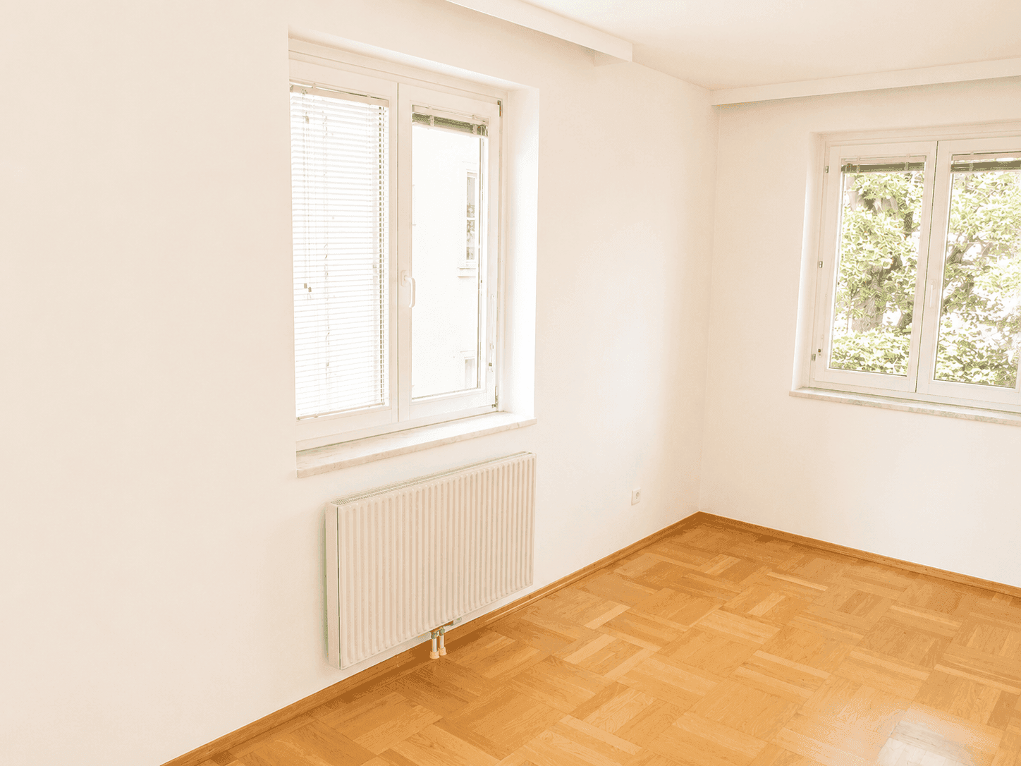 Ruhiges Zimmer mit Parkettboden und zwei Fenstern, die für ausreichend Tageslicht sorgen.