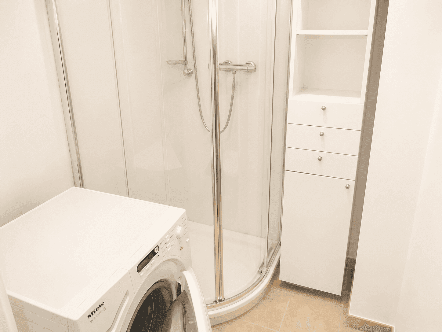 Funktionales Badezimmer mit Duschkabine und Waschmaschine, ideal für den täglichen Gebrauch.