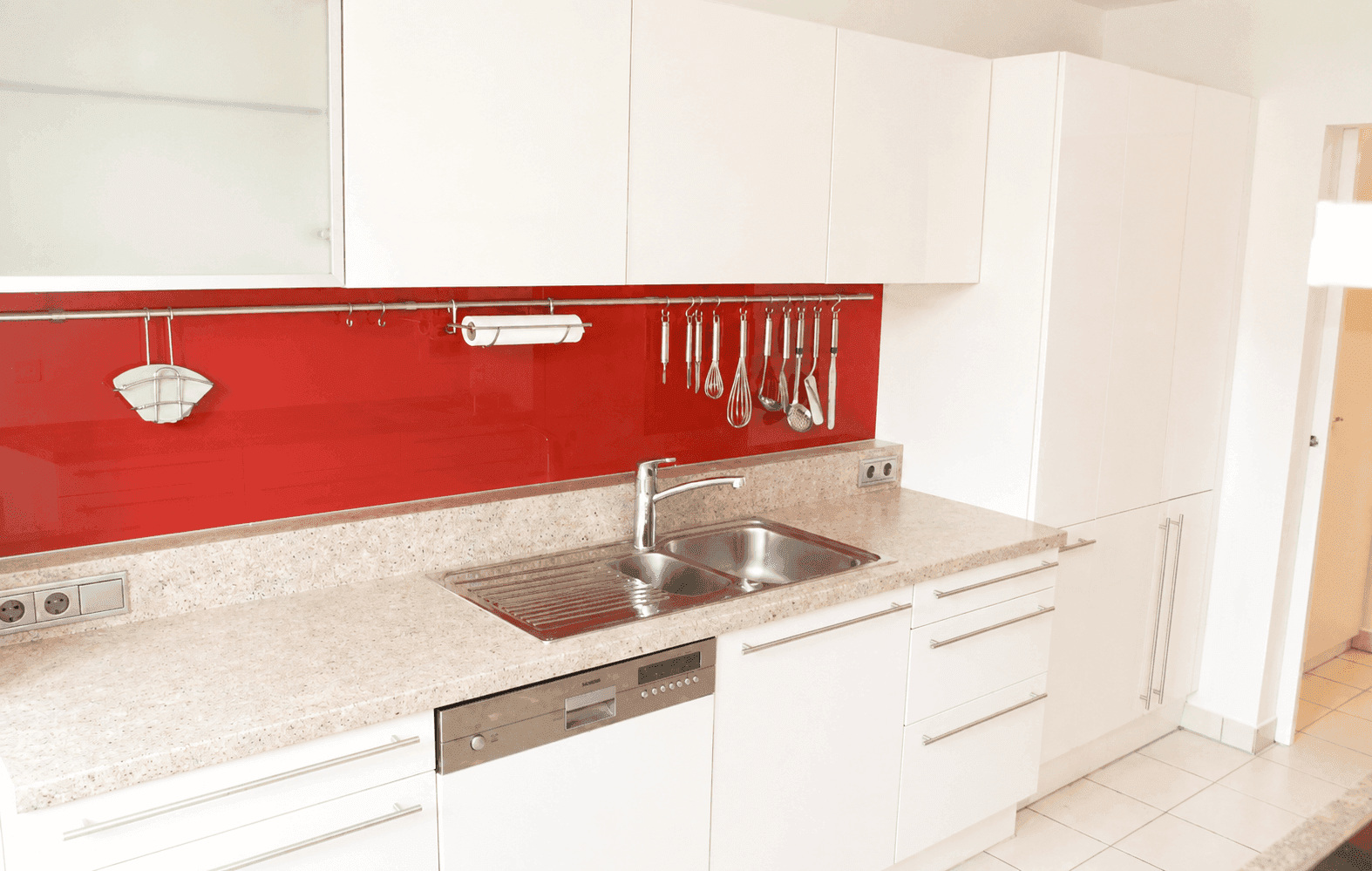Moderne Einbauküche mit weißen Hochglanzfronten, roter Rückwand und integriertem Geschirrspüler.
