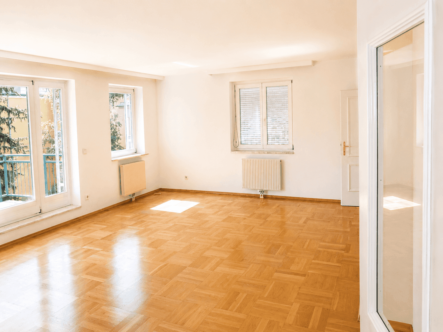 Geräumiges, helles Zimmer mit Parkettboden und mehreren Fenstern, die viel Licht hereinlassen.
