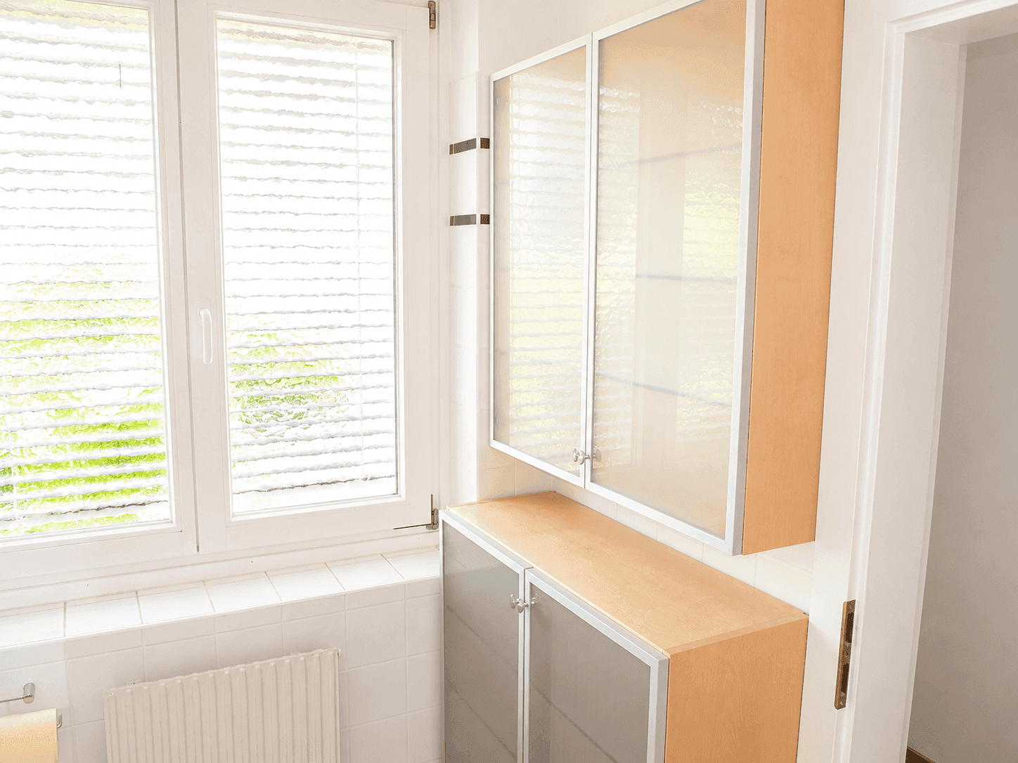 Helles Badezimmer mit Fenster, weißen Fliesen und praktischen Schränken für Stauraum.