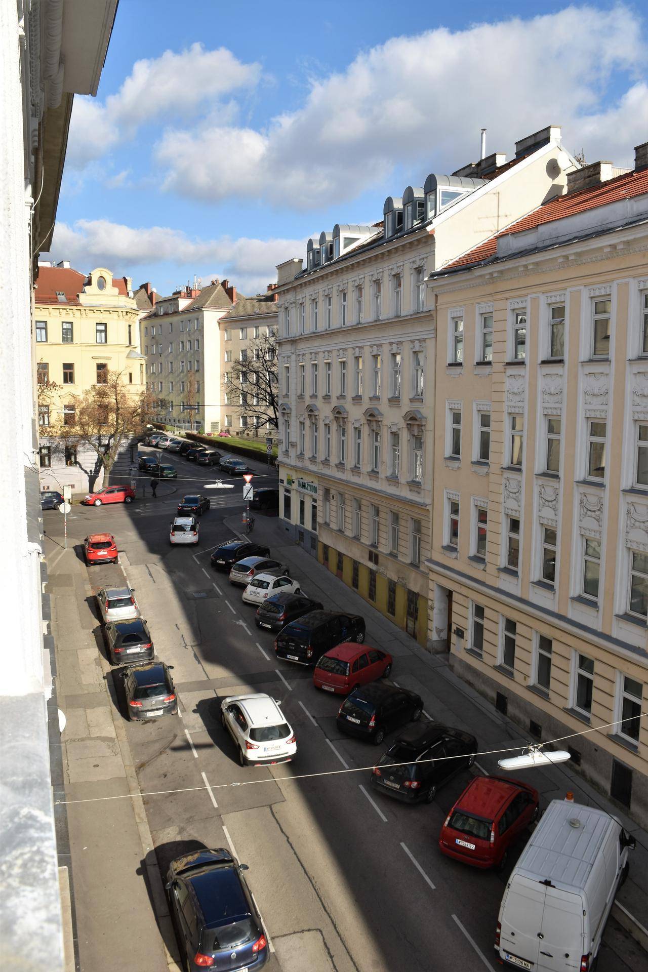 Blick von oben auf eine belebte Straße mit parkenden Autos und umliegenden Wohngebäuden.
