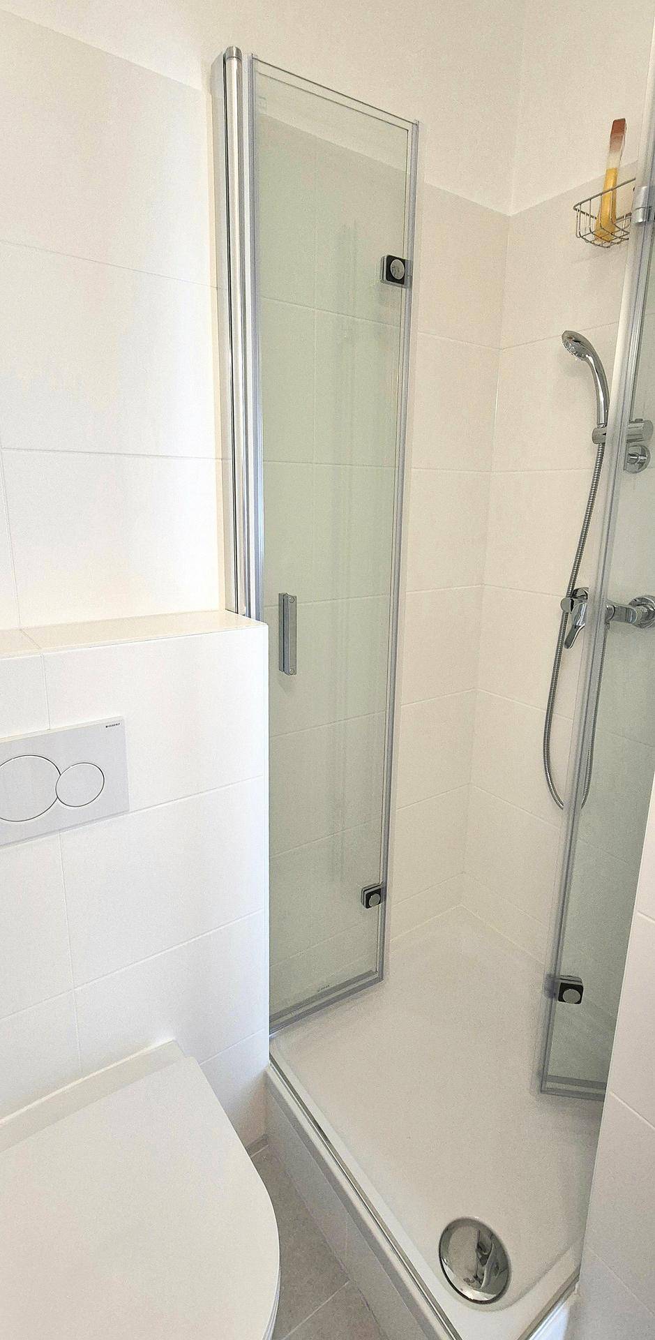 Duschbereich im Badezimmer mit Glasabtrennung und hellen Fliesen, sauber und funktional gestaltet.