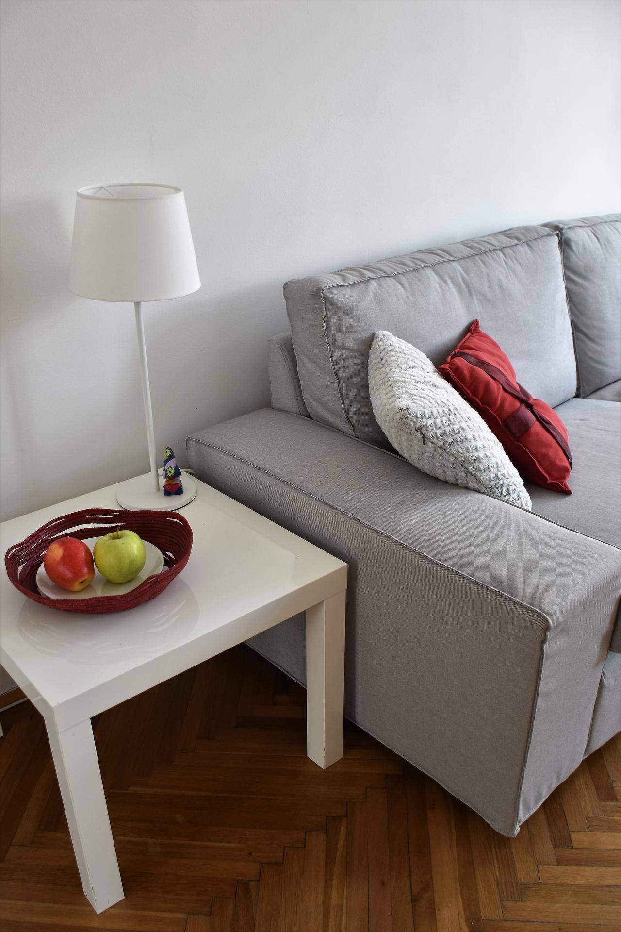 Detailansicht der Couch mit Beistelltisch, Lampe und Obstschale, auf elegantem Fischgrätparkett.