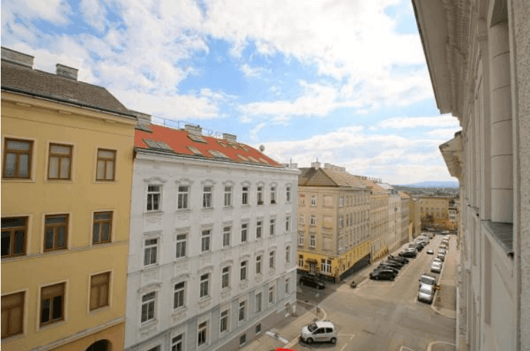 Weitläufiger Blick über eine städtische Straße mit historischen Gebäuden unter blauem Himmel.