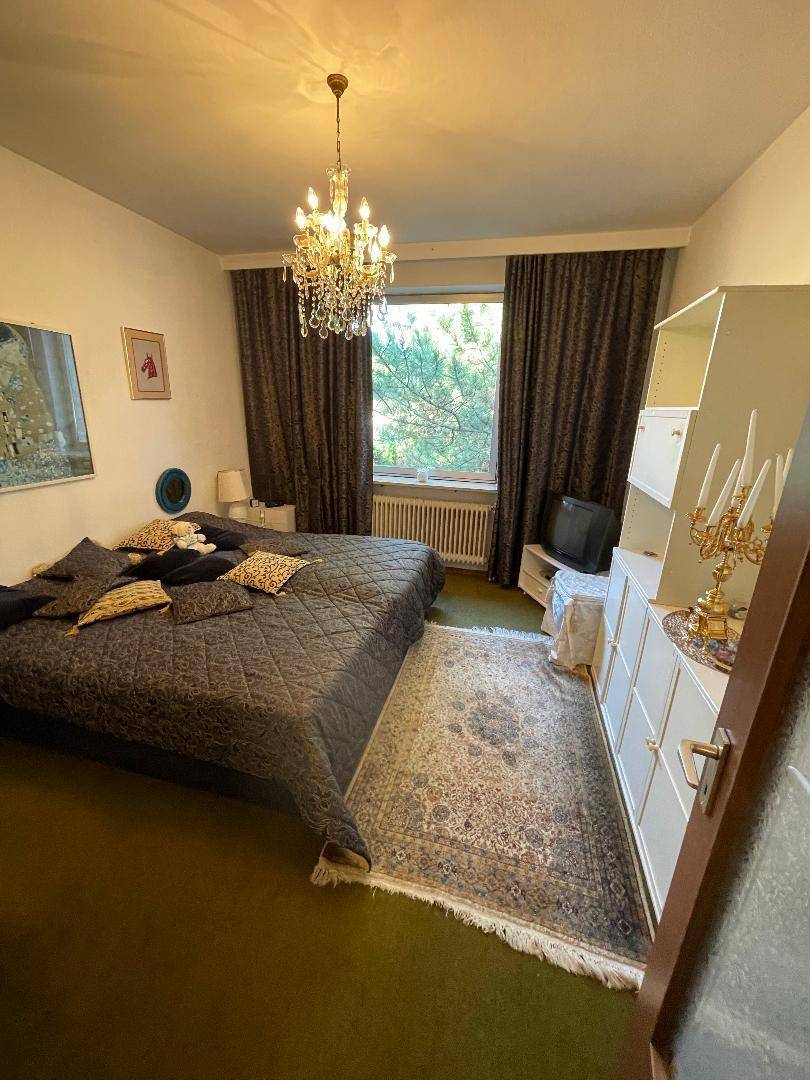 Schlafzimmer mit großem Bett, Kleiderschrank, Kronleuchter und Blick ins Grüne.