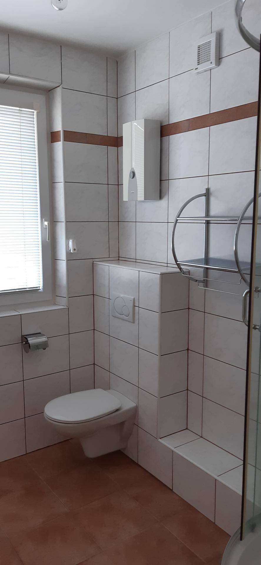 Modern gefliestes Badezimmer mit wandhängendem WC, Dusche und Fenster.