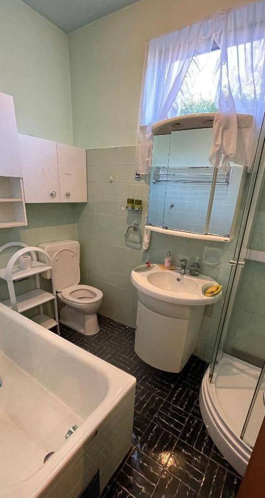 Badezimmer mit Badewanne, Dusche, WC und Fenster, ausgestattet mit hellblauen Fliesen.
