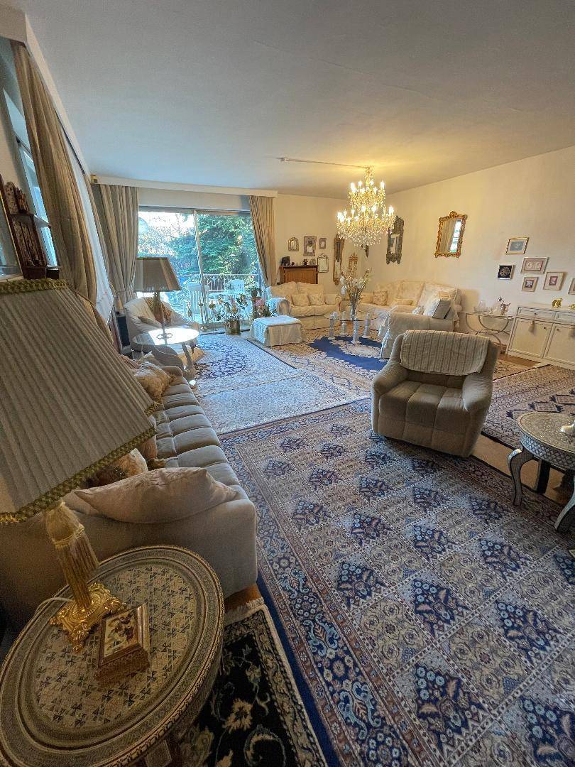 Großzügiges Wohnzimmer mit mehreren Sitzbereichen, Kronleuchter und Zugang zu einem Außenbereich.