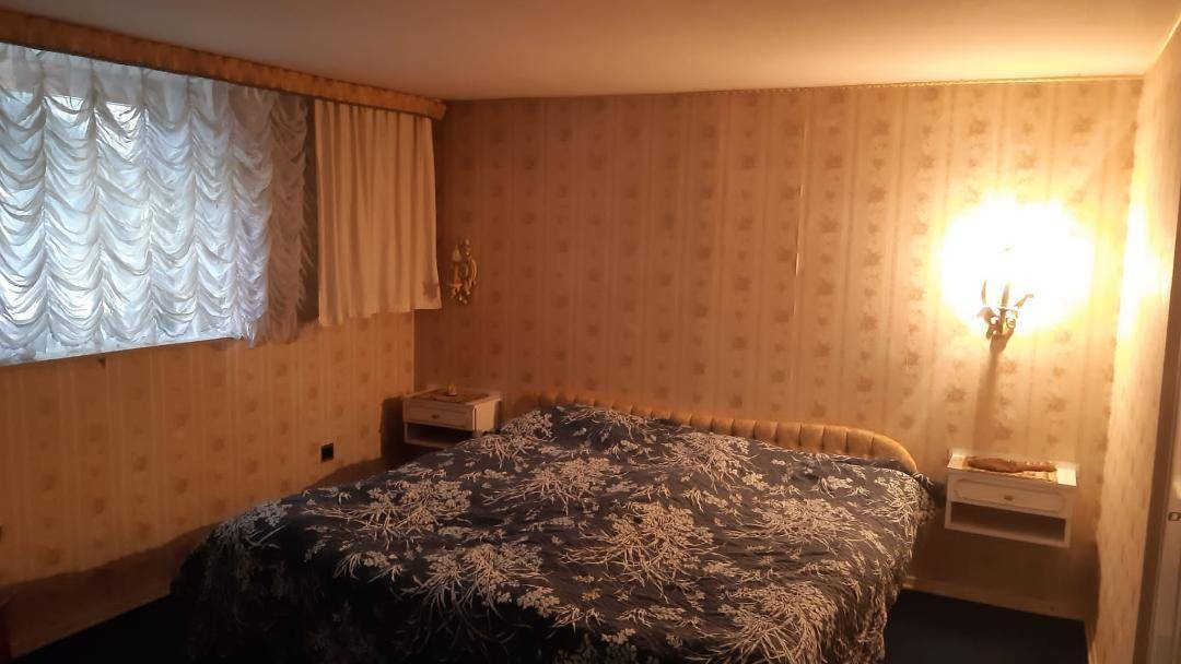 Schlafzimmer mit gemusterter Tapete, Doppelbett und Nachttischen, in gedämpftem Licht.