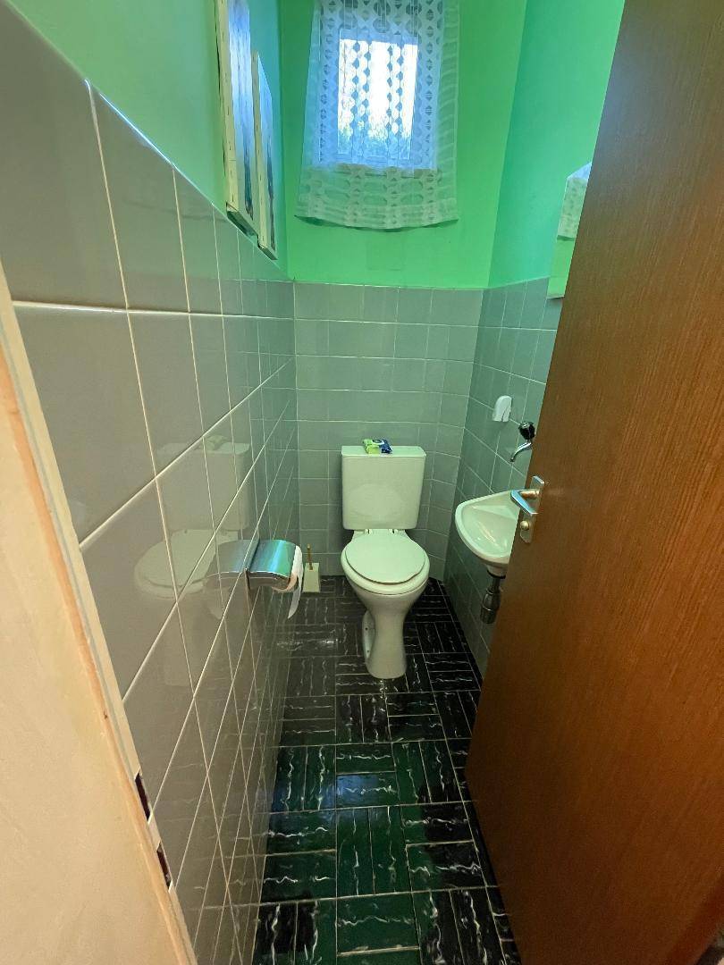 Kleines Gäste-WC mit grünen Wänden, dunklen Fliesen und einem Fenster für natürliche Belüftung.
