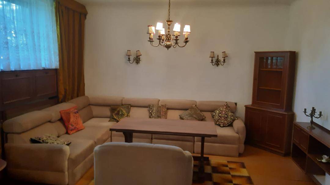 Geräumiges Wohnzimmer mit beigem Ecksofa, Couchtisch und traditionellen Holzmöbeln.