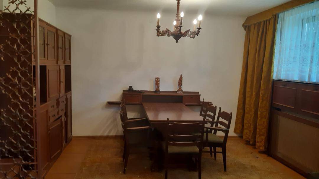 Klassisches Esszimmer mit großem Holztisch, passenden Stühlen und einem Fenster mit Vorhängen.