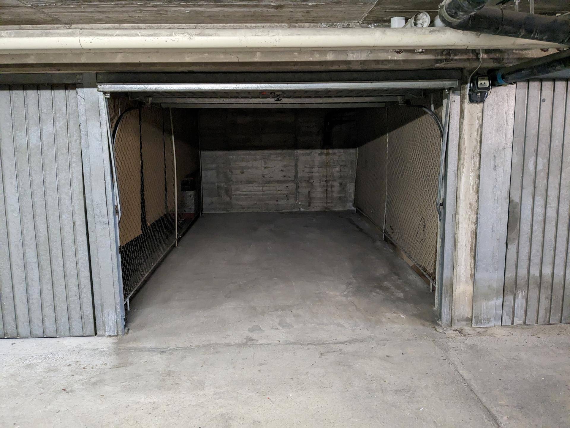 Offenes Garagentor zeigt einen leeren Stellplatz in einer Tiefgarage mit Betonwänden und Gitterabtrennungen.