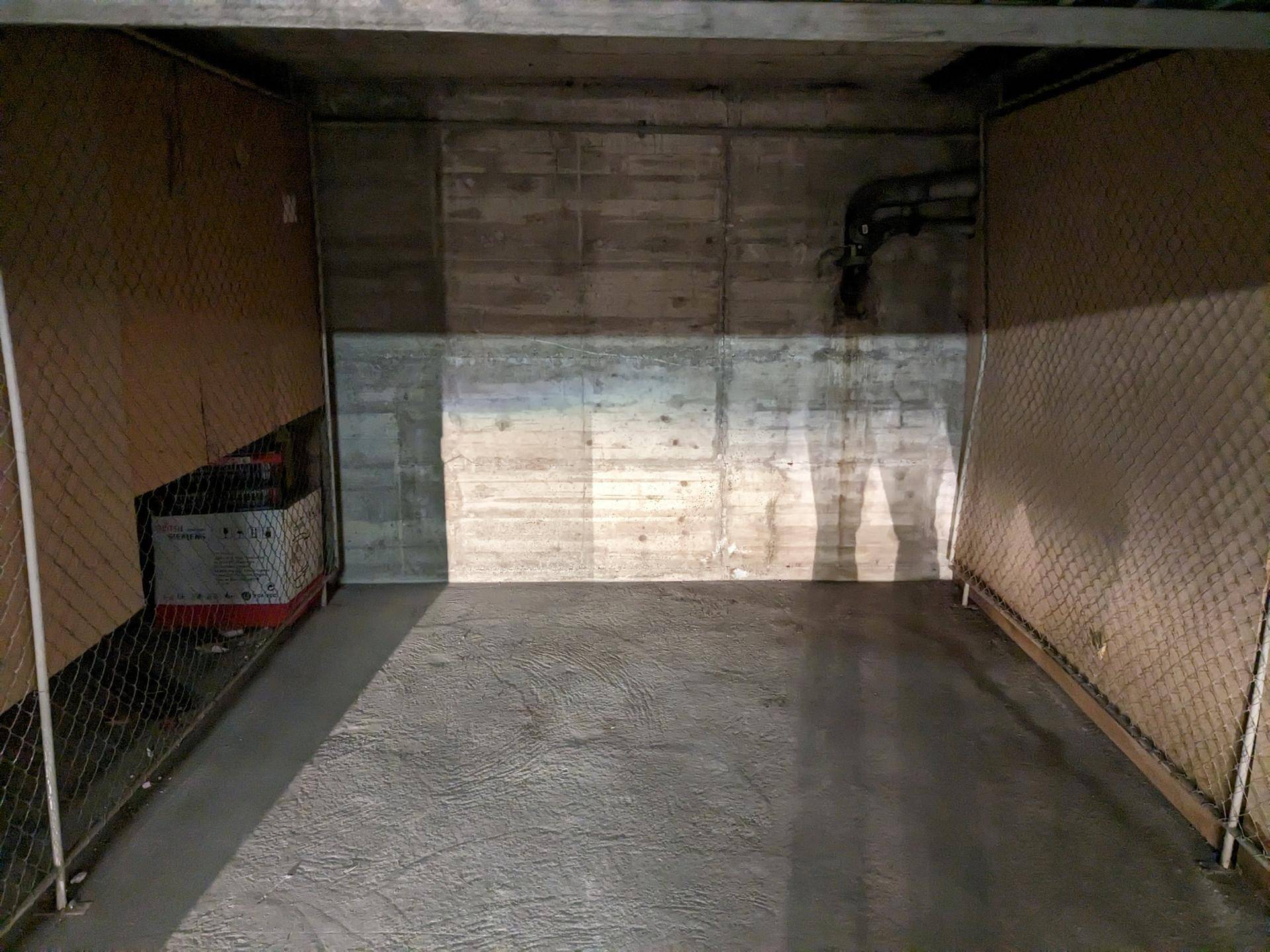 Innenansicht eines individuellen Garagenstellplatzes mit Betonwänden, Gitterabtrennungen und Lagerfläche.